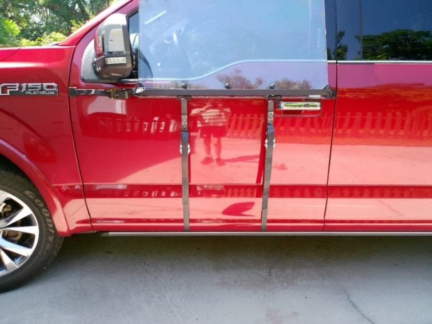 A red pickup with a clear WHIP guard hung over the driver's door window, held by two straps running down the door